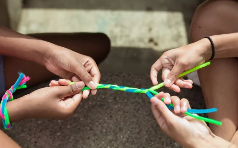 Close-up of kids making vibrant yarn bracelets at summer camp, focusing on hands and creativity.