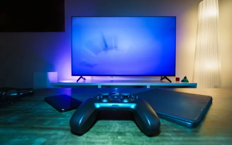 A stylish and ambient gaming setup featuring a controller, smart devices, and a TV in a lit living room.