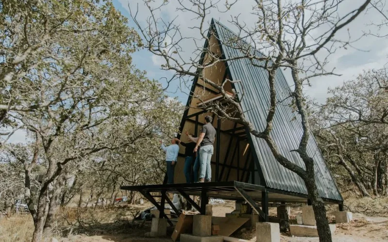 A group of people constructing a modern A-frame cabin in a forest.