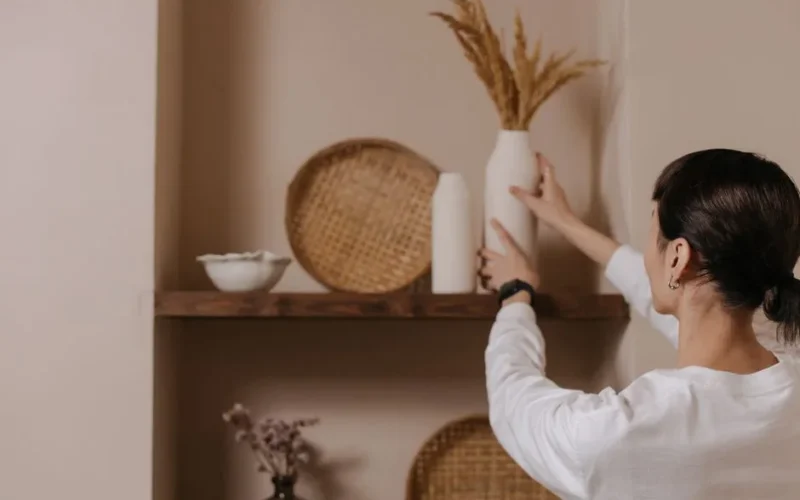 A woman arranging vases on a rustic shelf, highlighting minimalist interior design.