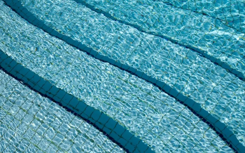 A detailed view of crystal clear swimming pool water over a tiled surface, showcasing its calm and refreshing nature.