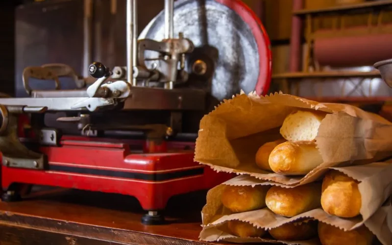 Warm bakery scene featuring fresh baguettes in paper bags beside a vintage slicer.