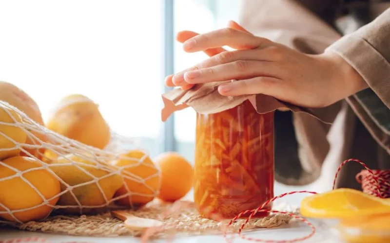 A jar of homemade orange marmalade with fresh oranges in a cozy kitchen setting.