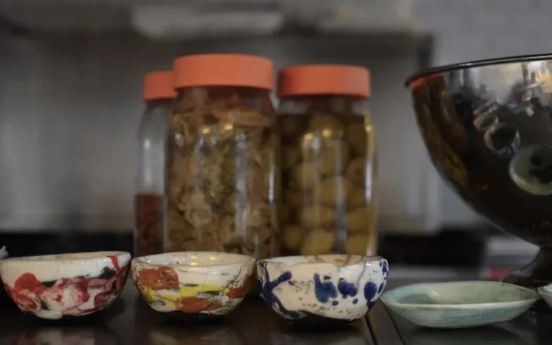 Artistic close-up of colorful ceramic bowls and jars of fermented food on a kitchen counter.