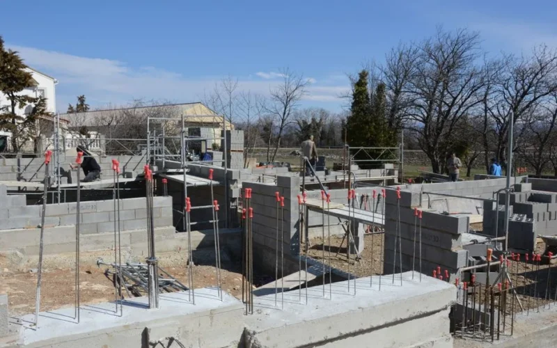 Sunlit construction site with workers on concrete foundation under a clear blue sky.