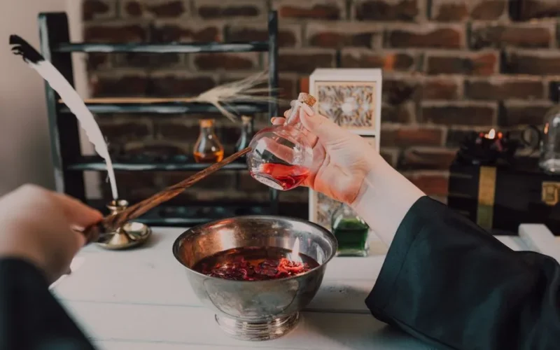 Hands crafting a magical potion with a wand and flask in a vintage setting.