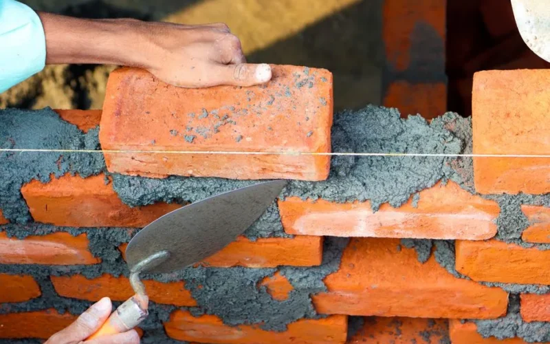 Hands laying bricks with cement in a construction setting, showcasing precise masonry work.