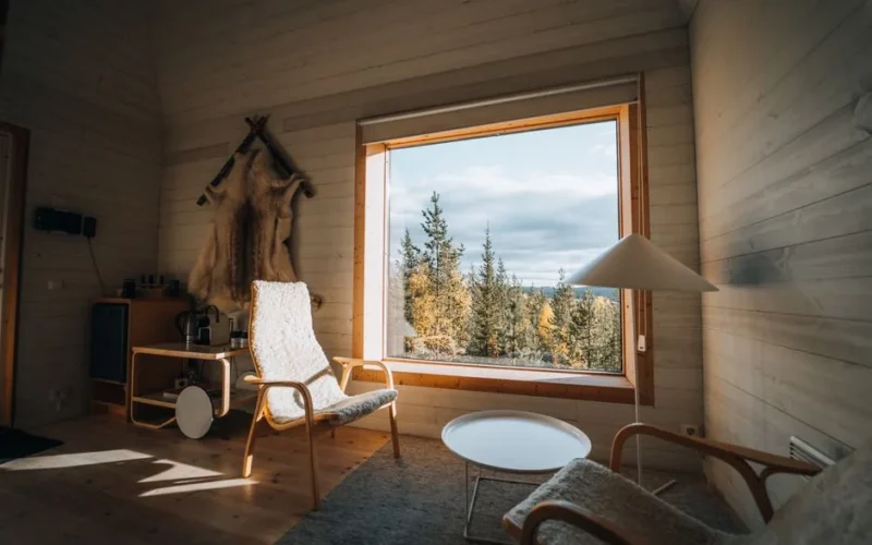 Warm cabin interior featuring natural wood decor and a large window overlooking a serene forest landscape.