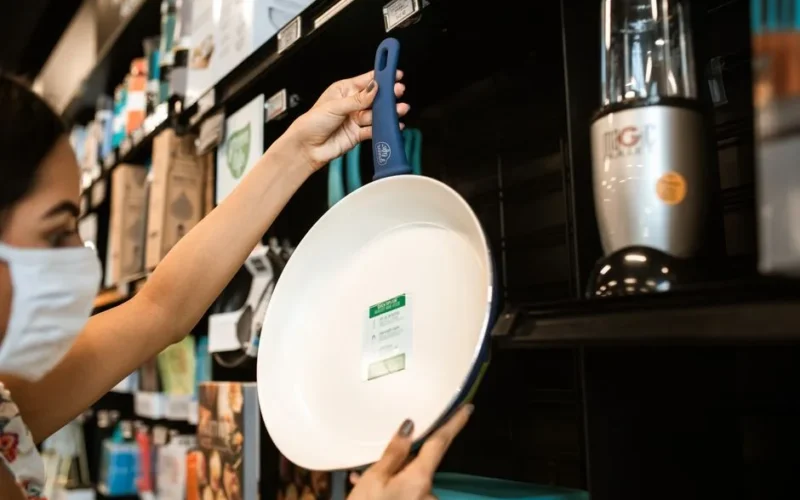 A woman in a mask shops for a frying pan at a store, a common pandemic scenario.