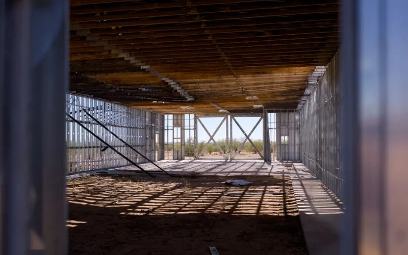 Interior view of a construction site with metal framing and wooden ceiling, under bright sunlight.