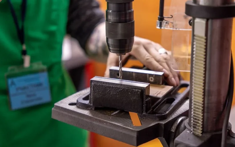 Detailed view of a hand operating a drill press in a workshop setting.