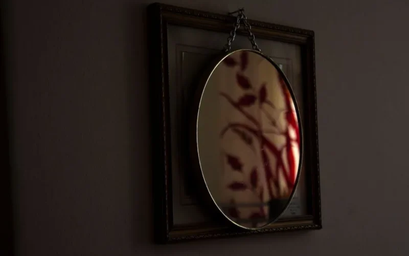 An oval mirror with chain hanging reflects abstract art, creating a moody atmosphere indoors.