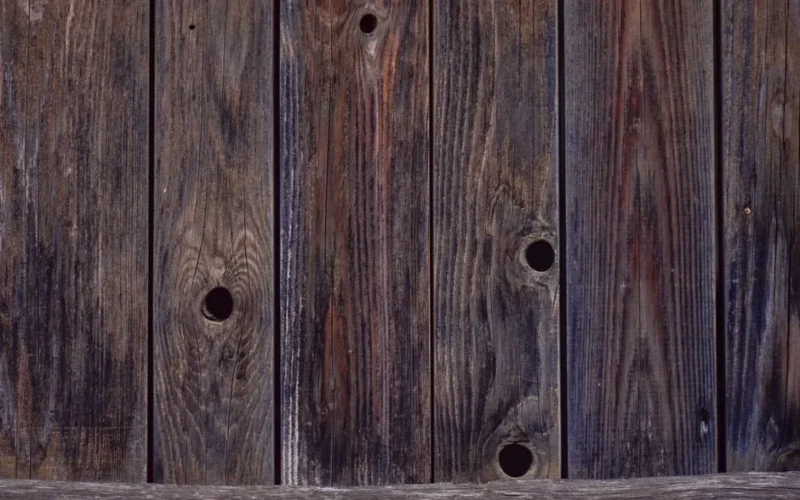 Close-up of weathered wooden planks with holes, ideal for rustic backgrounds.