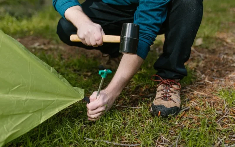 Close-up of a person hammering a tent peg into the ground during a camping trip.