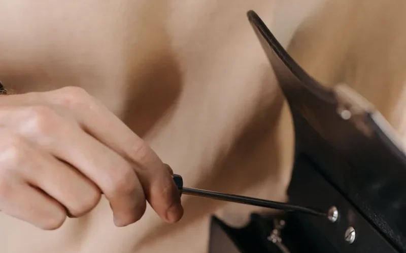 Close-up of hand using screwdriver to craft a detailed leather bag.