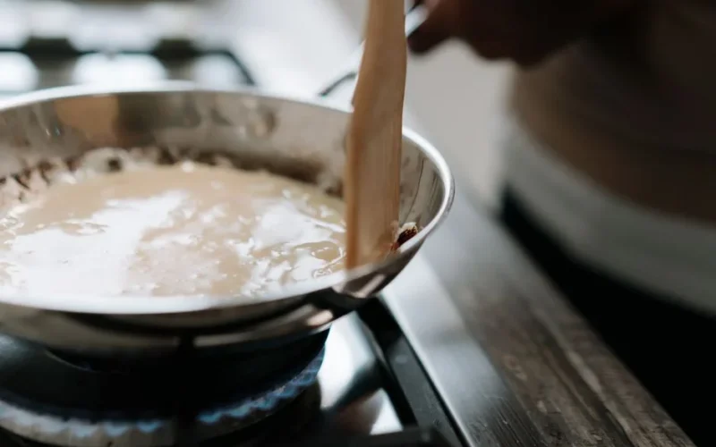 A close-up of sauce being stirred in a pan on a stove, highlighting cooking techniques.