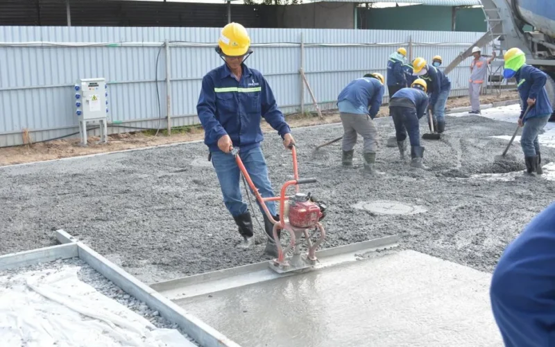Team of workers smoothing and leveling wet concrete at a construction site.