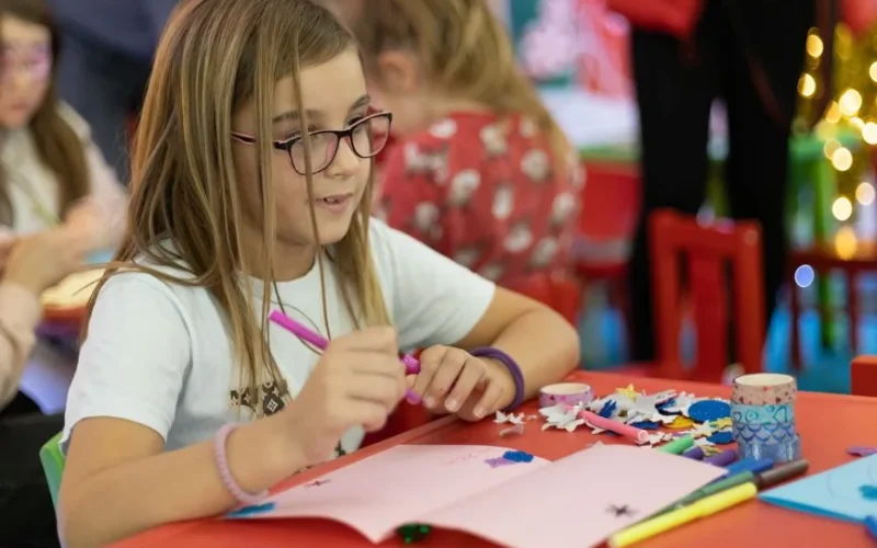 Young girl crafting a Christmas card with colorful materials during a holiday celebration.