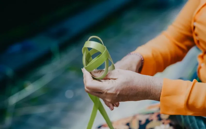 Close-up of elderly hands weaving a palm leaf basket outdoors, highlighting traditional craftsmanship.