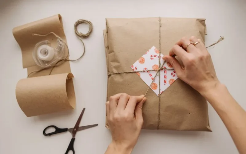 Hands tying a brown paper wrapped package with string, showcasing DIY gift wrapping.