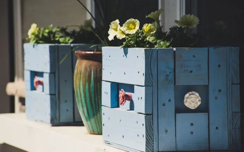 Charming blue wooden planter boxes filled with flowers on a sunlit porch, perfect for home decor inspiration.