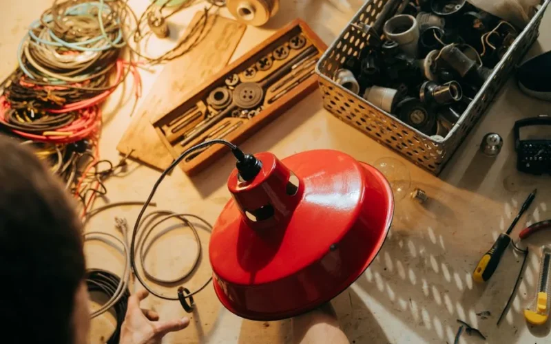 Overhead view of a workshop showing tools, wires, and a red lamp being assembled.