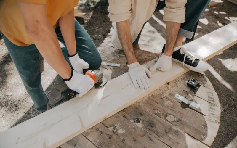 Two young carpenters using electric tools on a wooden plank outdoors. Practical DIY woodworking scene.