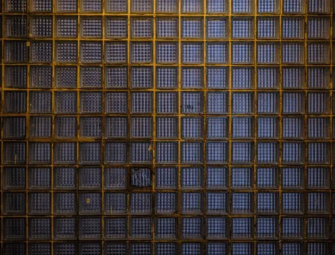 Detailed view of a textured glass brick wall with a metal grid, showcasing geometric patterns and industrial design.