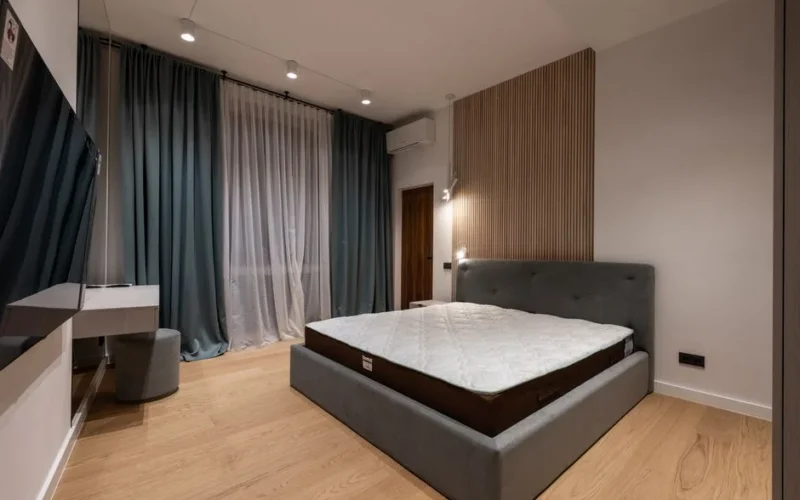 Modern TV set and comfy bed in stylish room decorated with lamps and curtains