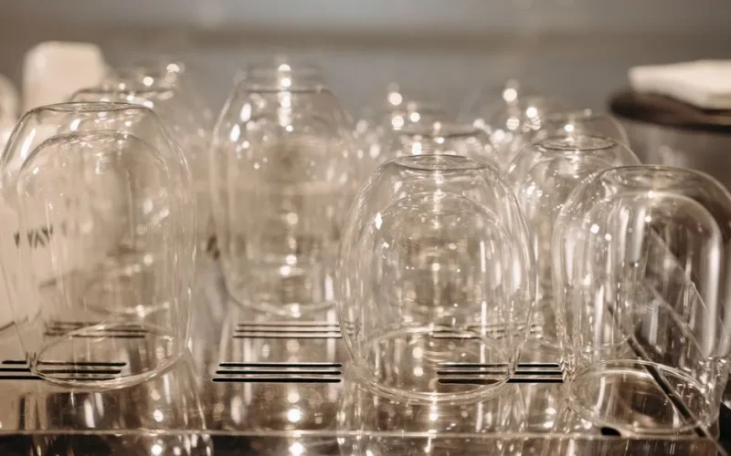 A collection of upside-down glasses drying on a stainless steel rack with soft lighting.