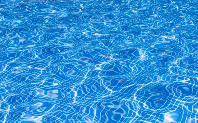 Bright blue swimming pool surface with sunlight reflecting in ripples and waves.