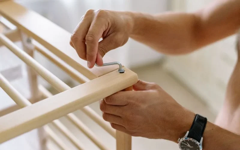 Close-up of a man using an Allen wrench to assemble a wooden baby cot indoors.