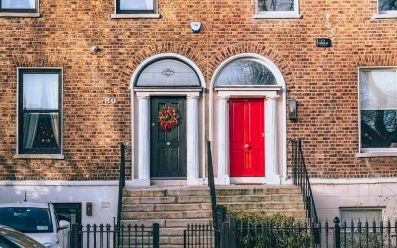 A classic brick facade featuring a bold red door and a decorated black door in an urban setting.