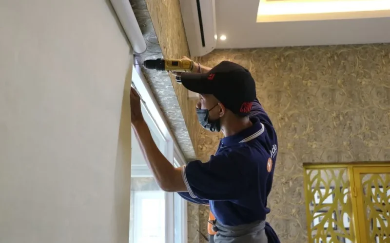 A worker using a drill to install window blinds in an indoor setting.