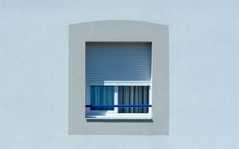 Simple and clean architectural window with roller blinds casting shadows on a plain wall.