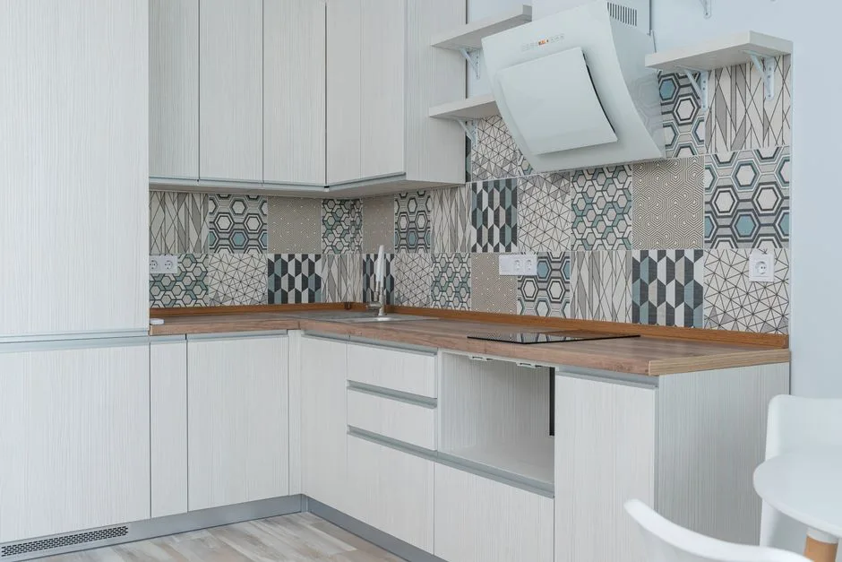 Interior of contemporary kitchen with white cabinets and wooden counter near ornamental tile on wall and modern appliances in apartment