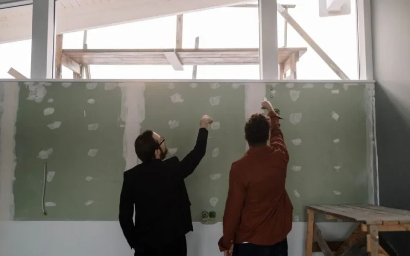 Two men discussing and pointing at an interior wall during a renovation project.