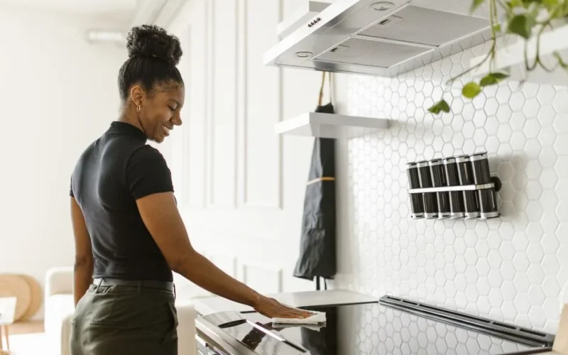 A woman cheerfully cleans her kitchen, focusing on the electric stove in a bright, modern space.