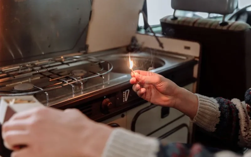 Close-up of hands lighting a matchstick near a stovetop in a cozy kitchen environment.
