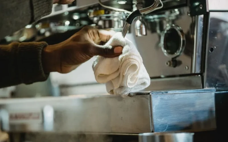 Close-up of a person cleaning a coffee machine using a cloth. Focus on hygiene and maintenance.
