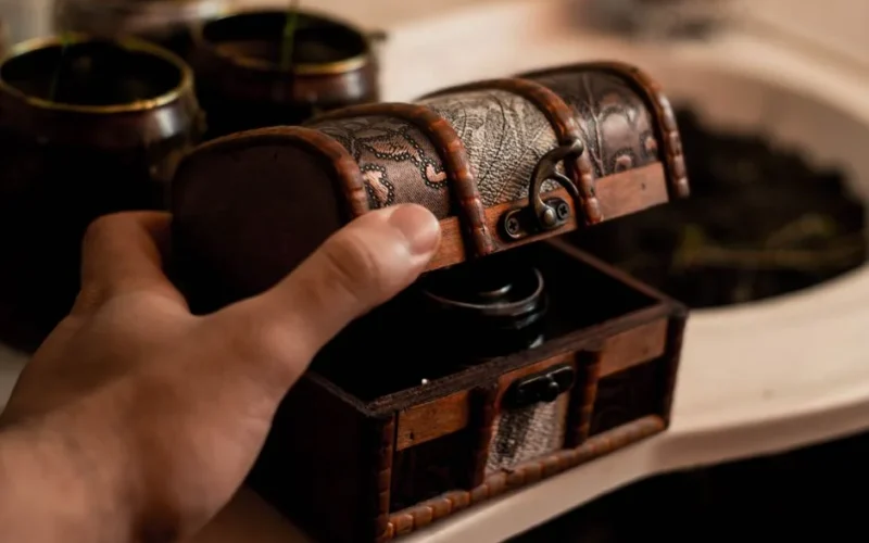 Crop anonymous male artisan opening small antique wooden chest placed on table at home