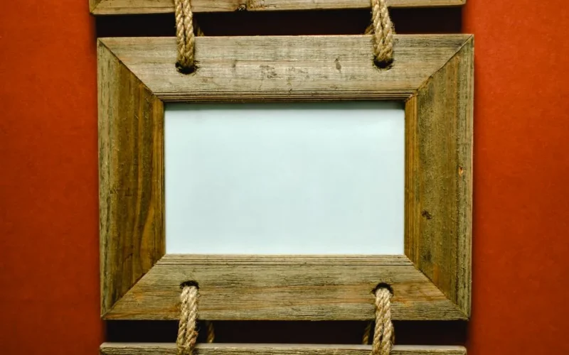 A rustic wooden photo frame with rope detail against a red background, perfect for decor themes.
