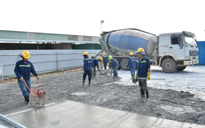 Team of workers pouring cement from a mixer truck on a construction site, ensuring proper leveling.