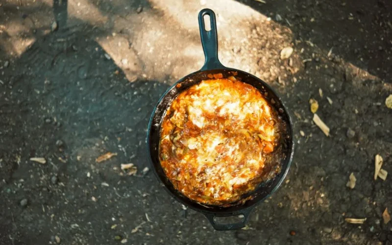 Delicious stew cooking in a cast iron skillet over open fire outdoors, perfect rustic meal.