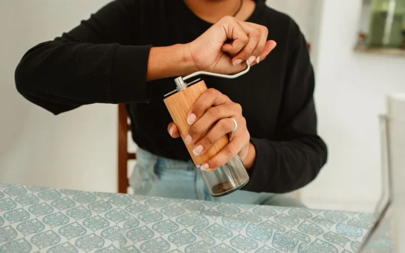 A person using a manual coffee grinder in a cozy indoor setting.