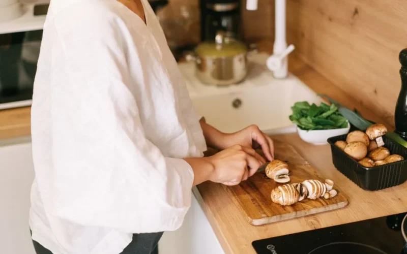 A person prepares mushrooms on a cutting board in a kitchen setting.