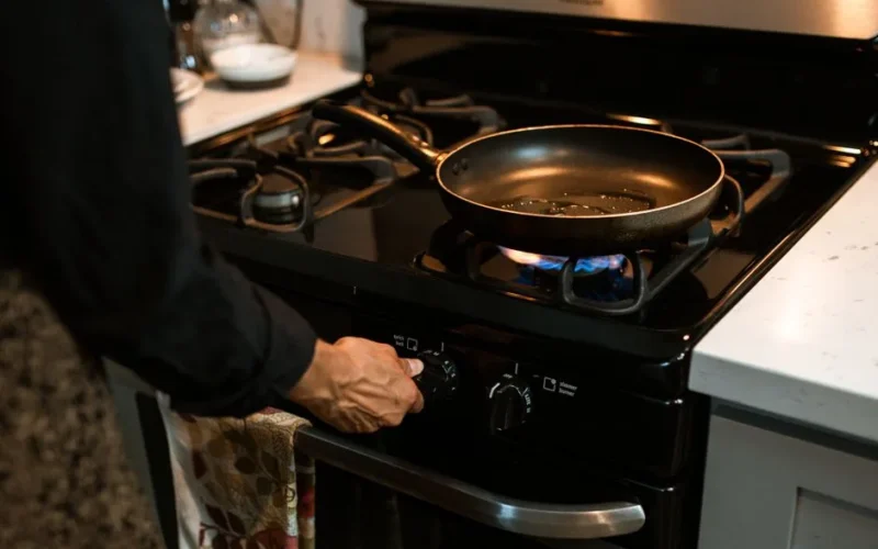 Crop unrecognizable housewife adjusting rotary switch of gas stove while cooking dinner in modern kitchen