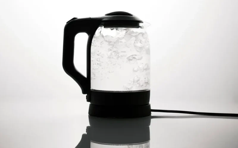 A sleek electric kettle boiling water, captured on a reflective white surface.