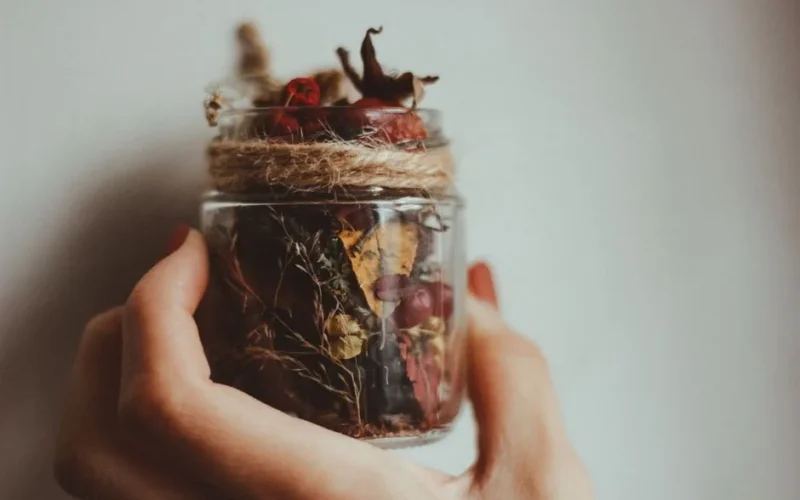 A hand holding a decorative jar filled with dried flowers and leaves, wrapped with twine.