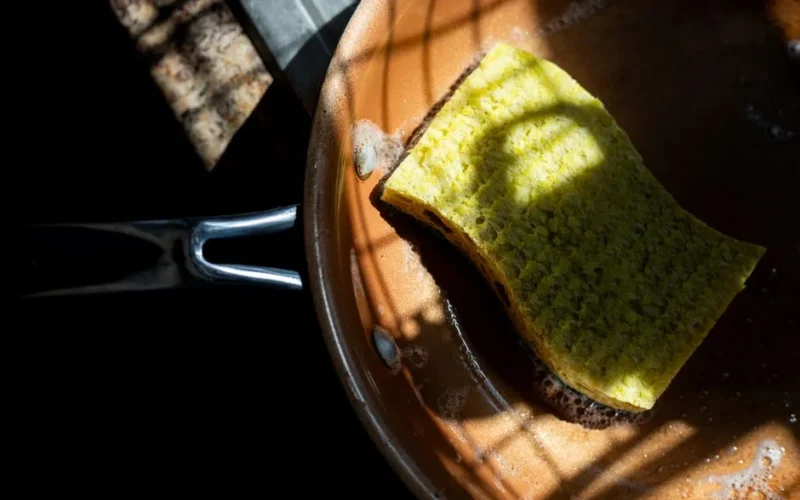 A yellow sponge rests in a copper pan, lit by dramatic shadows. Ideal for cleaning themes.
